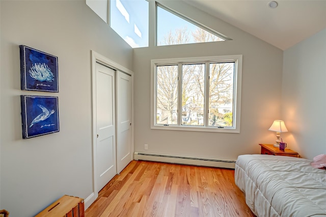 bedroom with lofted ceiling, a closet, baseboard heating, and light hardwood / wood-style flooring