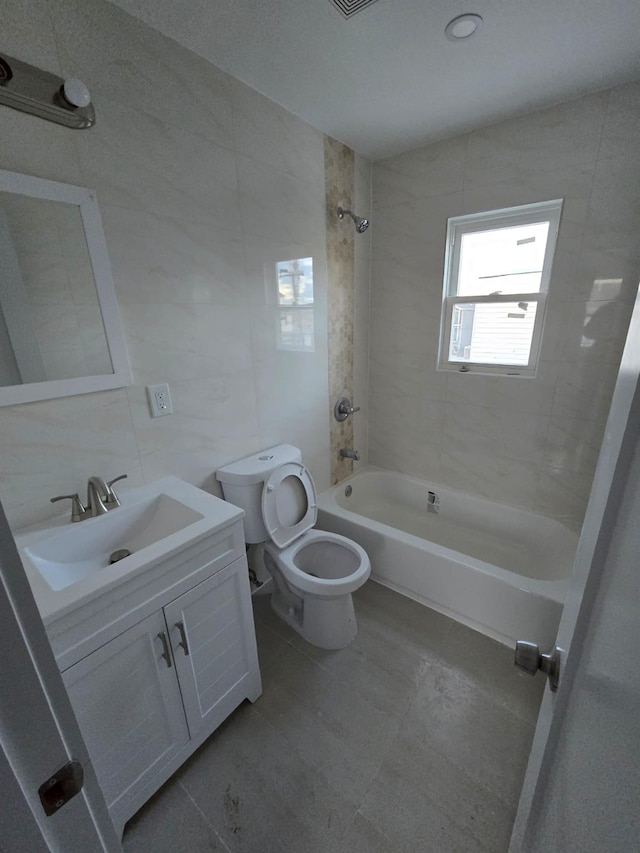 full bathroom featuring vanity, tiled shower / bath, tile patterned flooring, toilet, and tile walls