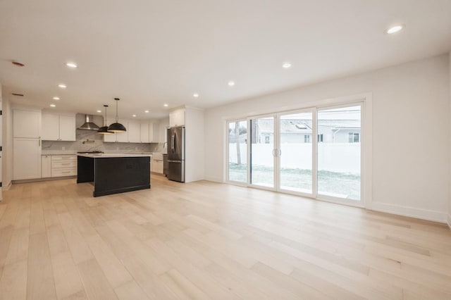 kitchen featuring a center island, wall chimney range hood, stainless steel fridge, pendant lighting, and white cabinets