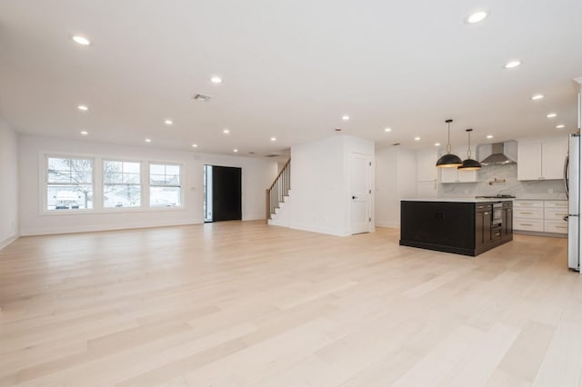 kitchen with white cabinets, a center island, wall chimney exhaust hood, and light wood-type flooring