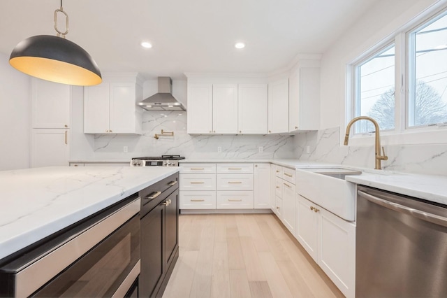 kitchen featuring dishwasher, white cabinetry, wall chimney range hood, and hanging light fixtures