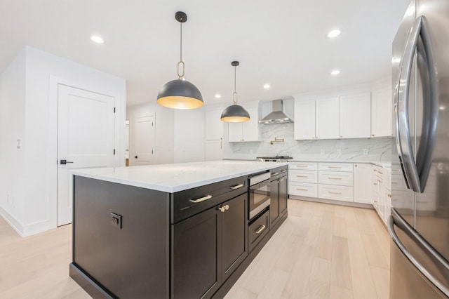 kitchen featuring white cabinetry, hanging light fixtures, stainless steel appliances, and wall chimney range hood