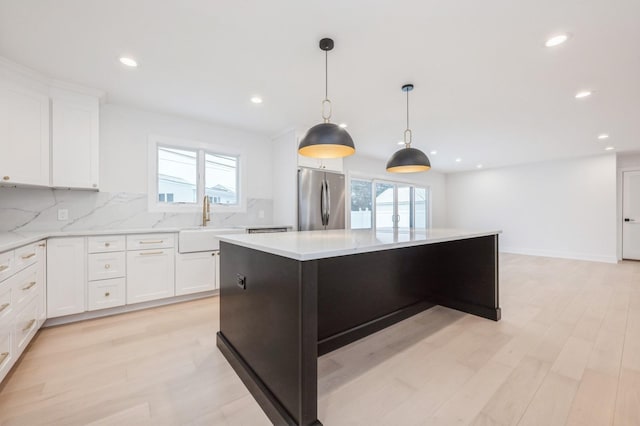 kitchen with stainless steel refrigerator, white cabinetry, sink, hanging light fixtures, and a kitchen island