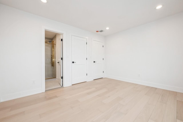 unfurnished bedroom featuring ensuite bathroom and light hardwood / wood-style flooring