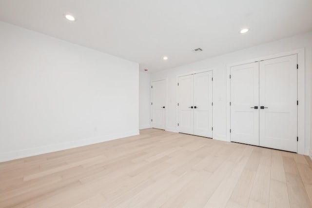 unfurnished bedroom with light hardwood / wood-style floors and two closets