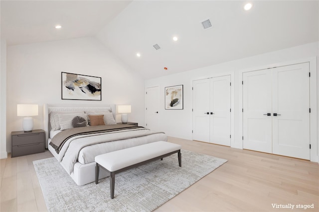 bedroom featuring two closets, light hardwood / wood-style floors, and high vaulted ceiling