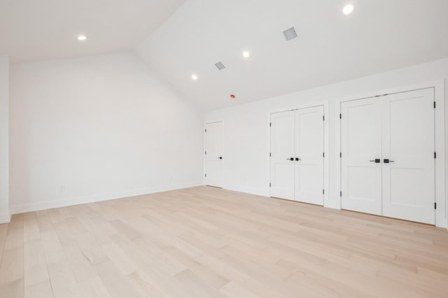 unfurnished bedroom with multiple closets, light hardwood / wood-style flooring, and vaulted ceiling