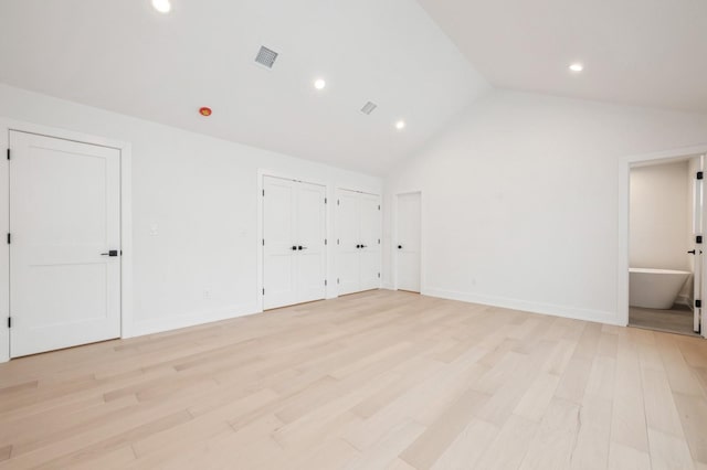 unfurnished bedroom featuring ensuite bathroom, vaulted ceiling, multiple closets, and light hardwood / wood-style floors