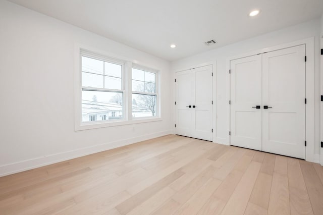 unfurnished bedroom with light hardwood / wood-style flooring and two closets