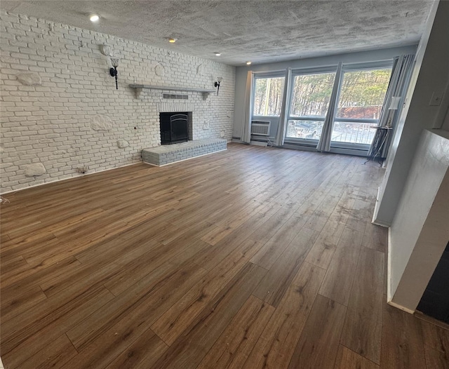 unfurnished living room featuring hardwood / wood-style flooring, a fireplace, brick wall, and a textured ceiling