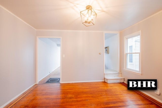 spare room featuring hardwood / wood-style flooring, crown molding, and a notable chandelier