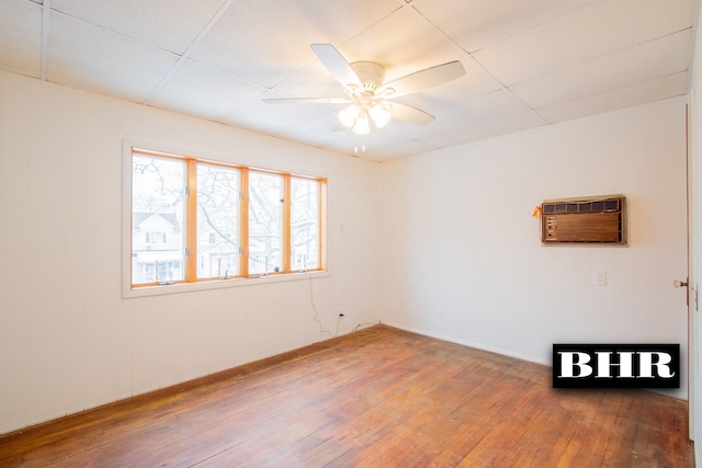 unfurnished room featuring a wall mounted air conditioner, hardwood / wood-style floors, a paneled ceiling, and ceiling fan