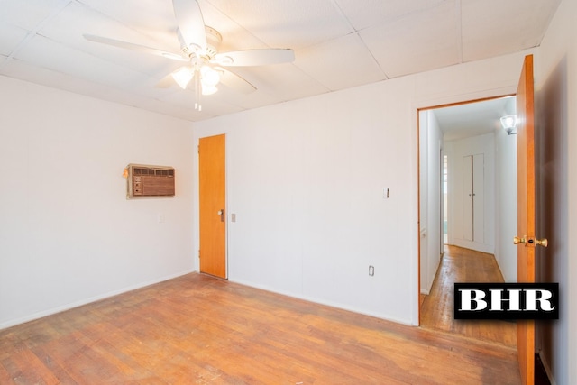 empty room featuring a paneled ceiling, ceiling fan, wood-type flooring, and an AC wall unit