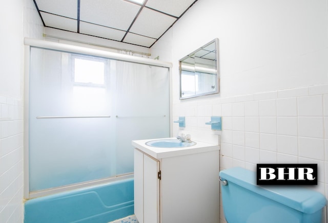 full bathroom featuring a paneled ceiling, vanity, toilet, enclosed tub / shower combo, and tile walls