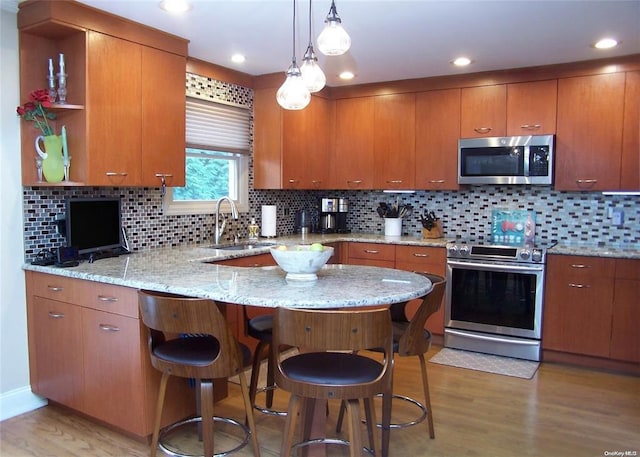 kitchen featuring sink, appliances with stainless steel finishes, light hardwood / wood-style floors, kitchen peninsula, and a breakfast bar area