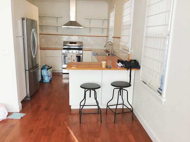 kitchen featuring sink, a breakfast bar area, wall chimney exhaust hood, kitchen peninsula, and stainless steel appliances