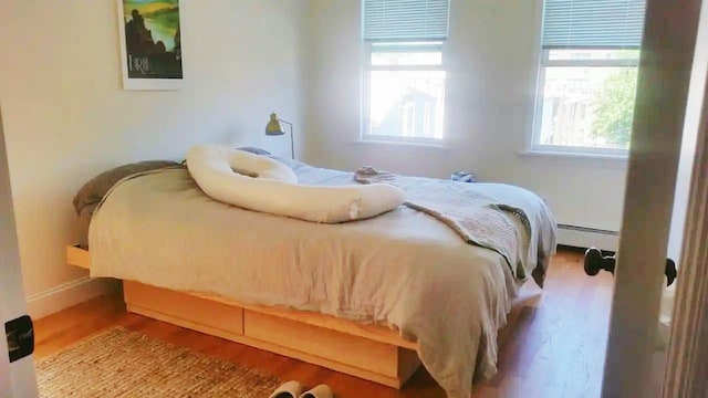 bedroom featuring multiple windows, light hardwood / wood-style flooring, and baseboard heating