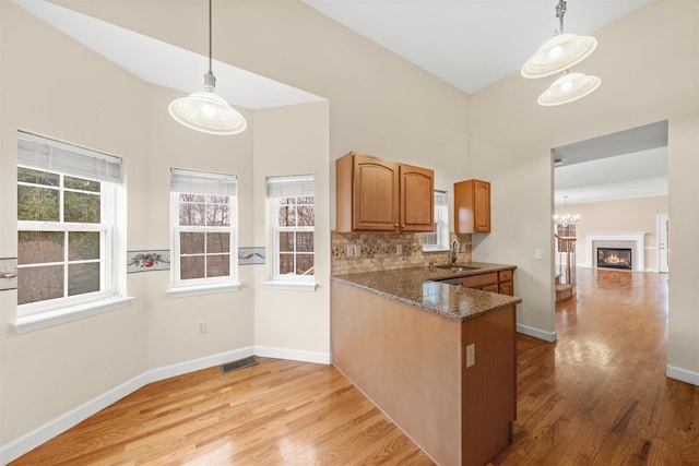 kitchen with sink, decorative light fixtures, dark stone countertops, tasteful backsplash, and kitchen peninsula