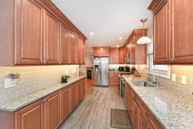 kitchen featuring appliances with stainless steel finishes, light stone counters, sink, decorative light fixtures, and light hardwood / wood-style floors