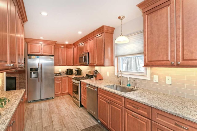 kitchen with light stone counters, stainless steel appliances, sink, pendant lighting, and light hardwood / wood-style floors