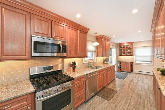 kitchen with sink, hanging light fixtures, decorative backsplash, light stone counters, and stainless steel appliances