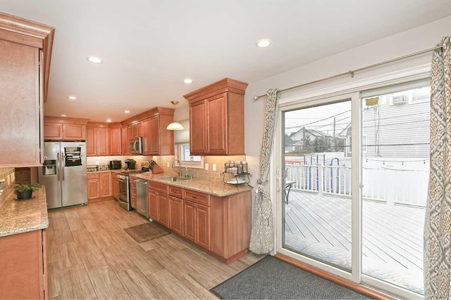 kitchen featuring light stone countertops, sink, light hardwood / wood-style flooring, decorative light fixtures, and appliances with stainless steel finishes