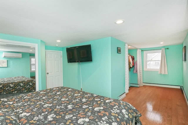 bedroom with light wood-type flooring, baseboard heating, and a wall mounted AC