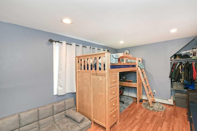 bedroom featuring a baseboard heating unit, wood-type flooring, and a closet