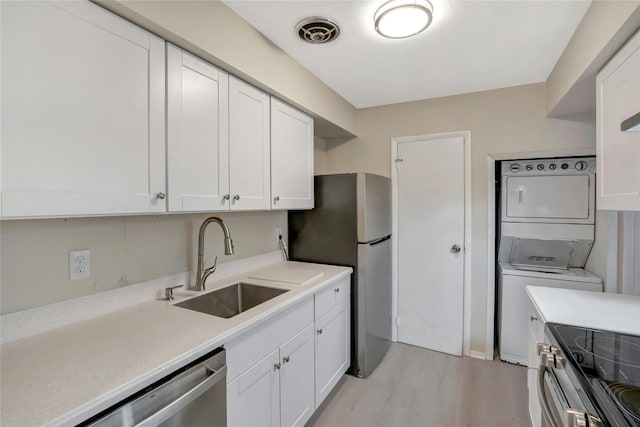 kitchen with sink, white cabinets, stainless steel appliances, and stacked washer / drying machine