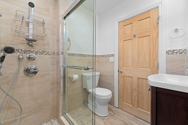 bathroom with vanity, toilet, a shower with door, and tile walls