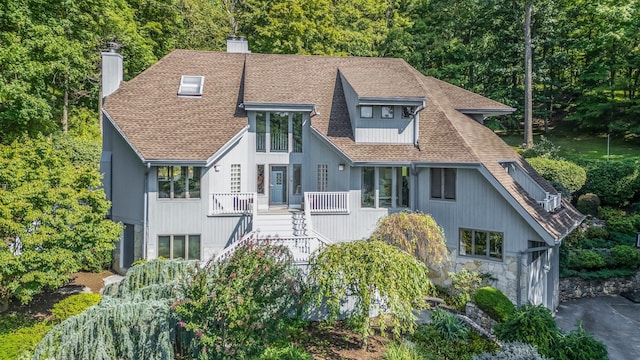 view of front of property with stairs, a shingled roof, a chimney, and a view of trees