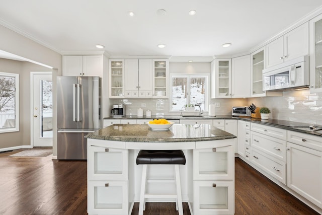 kitchen featuring white microwave, high end refrigerator, dark wood finished floors, a center island, and a kitchen bar