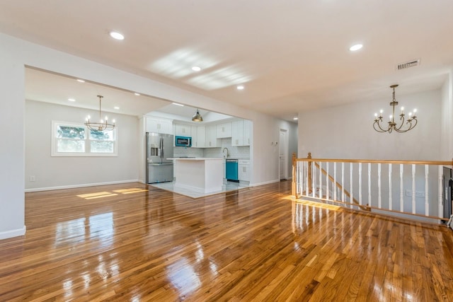 unfurnished living room with light wood-type flooring, an inviting chandelier, and sink