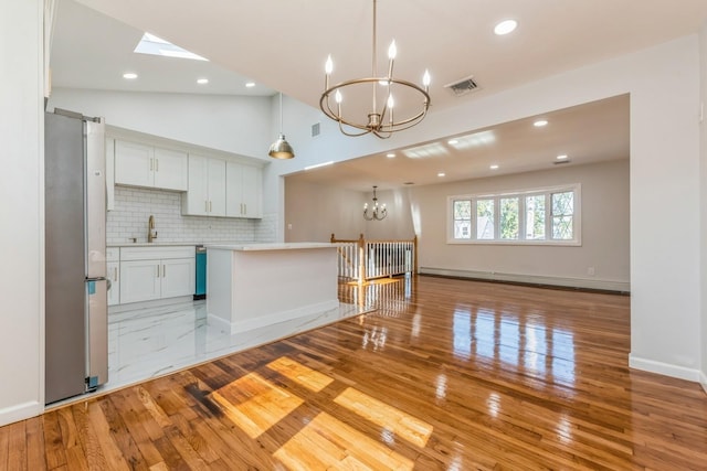 kitchen with pendant lighting, a baseboard heating unit, white cabinets, decorative backsplash, and stainless steel fridge