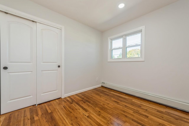 unfurnished bedroom with a baseboard radiator, a closet, and hardwood / wood-style flooring