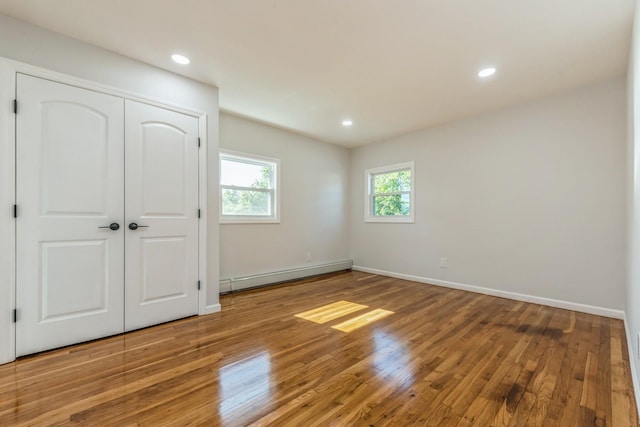 unfurnished bedroom with hardwood / wood-style flooring, a closet, and a baseboard heating unit