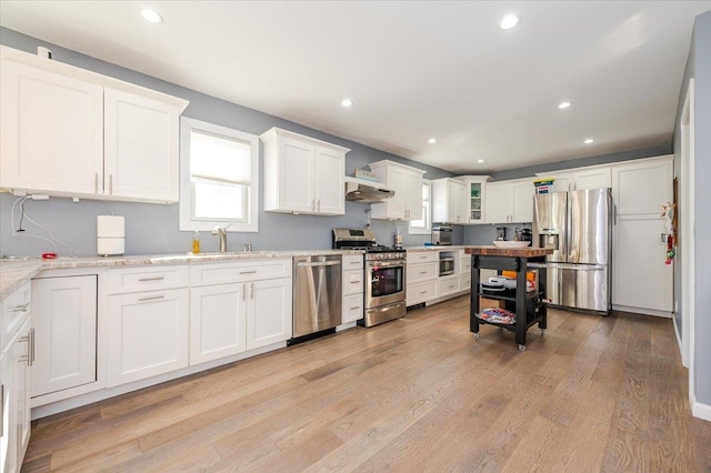 kitchen with light stone counters, stainless steel appliances, light hardwood / wood-style flooring, white cabinets, and range hood