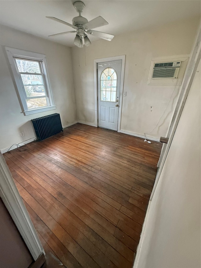 entryway featuring baseboards, a wall mounted air conditioner, radiator heating unit, hardwood / wood-style flooring, and a ceiling fan