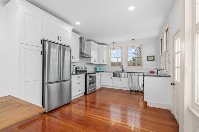 kitchen with stainless steel appliances, white cabinets, decorative light fixtures, and wall chimney range hood