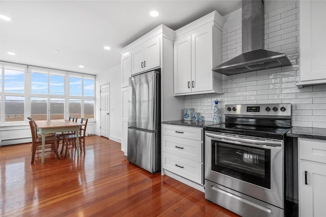 kitchen with white cabinets, wall chimney exhaust hood, stainless steel appliances, and dark stone countertops