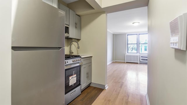 kitchen featuring radiator, hardwood / wood-style flooring, gray cabinets, and appliances with stainless steel finishes