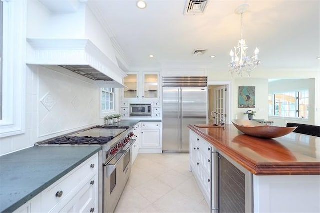 kitchen with wine cooler, built in appliances, crown molding, pendant lighting, and white cabinets