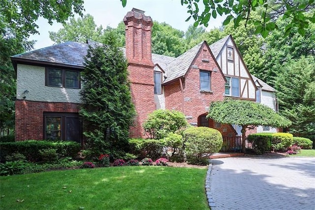 english style home with brick siding, a front yard, and a chimney