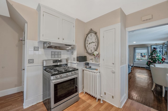 kitchen with radiator, stainless steel gas stove, extractor fan, light hardwood / wood-style floors, and white cabinets