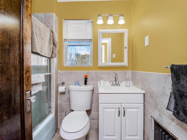 full bathroom with vanity, toilet, combined bath / shower with glass door, and tile walls