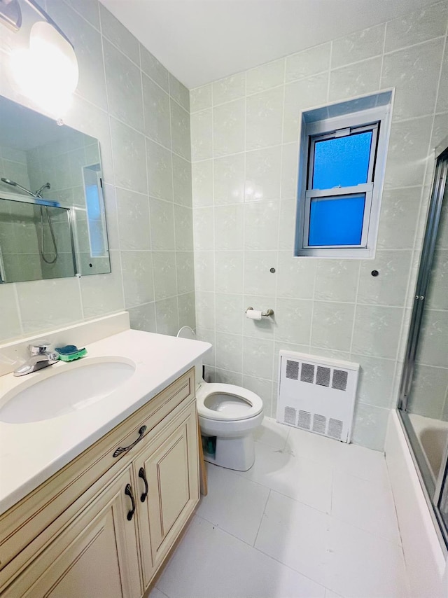 full bathroom with radiator heating unit, enclosed tub / shower combo, toilet, vanity, and tile walls