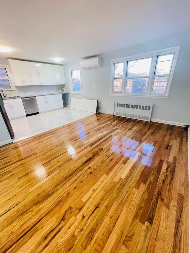 unfurnished living room with radiator heating unit, light hardwood / wood-style floors, and an AC wall unit