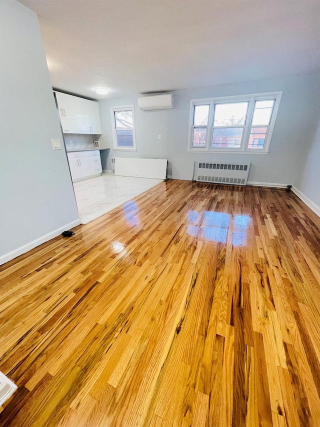 unfurnished living room featuring radiator, light hardwood / wood-style floors, and a wall mounted air conditioner