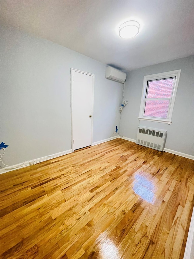 empty room featuring a wall mounted air conditioner, hardwood / wood-style flooring, and radiator