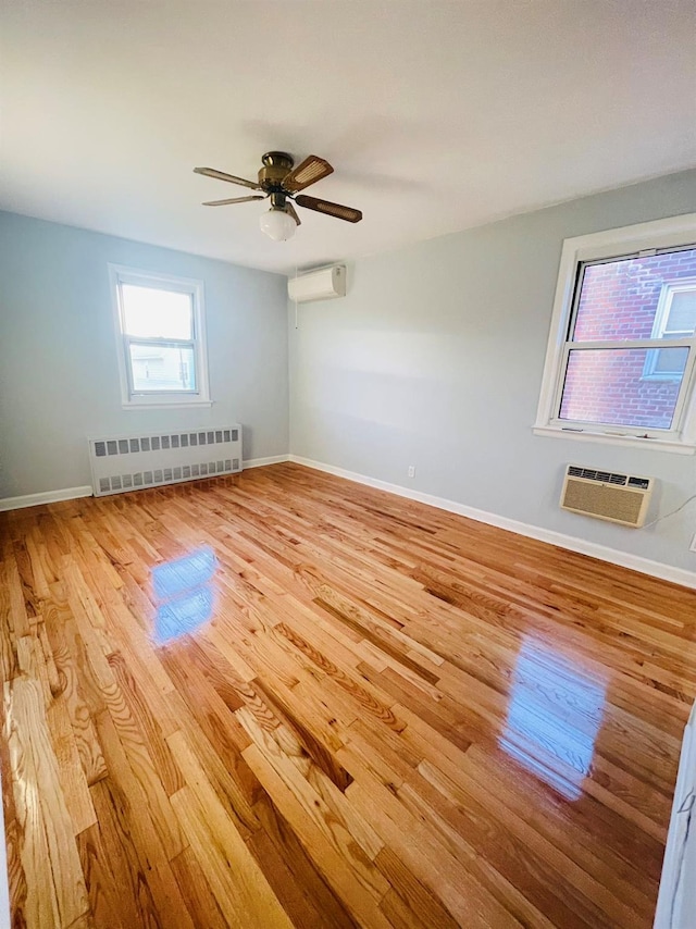 spare room featuring radiator heating unit, light hardwood / wood-style flooring, a wall mounted AC, and ceiling fan